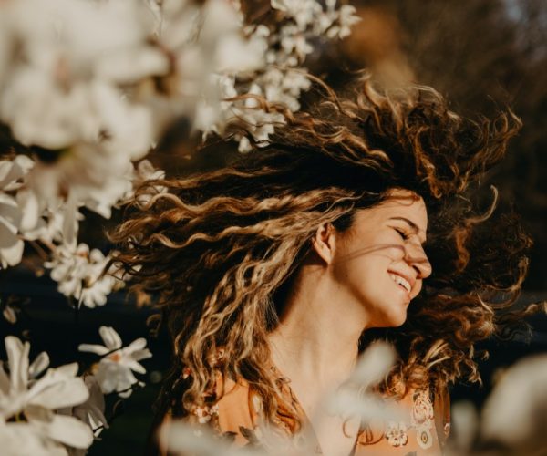 smiling woman living her best life and flipping her hair in a field of flowers